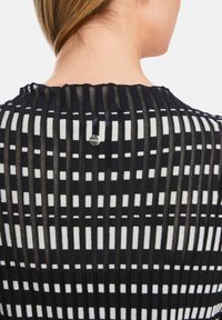 Gestreiftes Top in Schwarz und Weiß mit gerippter Textur und rundem Ausschnitt. Ein kleines silbernes Knopfdetail befindet sich auf der Rückseite.