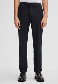 Pantaloni neri, slim fit, realizzati in tessuto intrecciato. Presentano una parte frontale piatta, passanti per la cintura e due tasche laterali. Abbinati a scarpe nere.