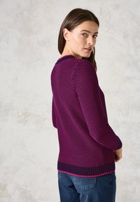 Pletený svetr v tmavě fialové barvě s texturovaným pleteným vzorem. Má kulatý výstřih, dlouhé rukávy a kontrastní ribbed lem.