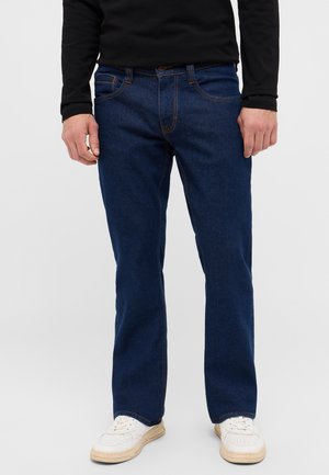 Blaue Jeans aus Denim mit geradem Schnitt, orangefarbenen Nähten und frontalen Taschen. Tragen Sie sie mit weißen Sneakers und einem schwarzen Langarmshirt.