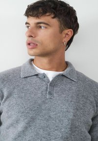 Graues Wollpolohemd mit klassischem Kragen, drei Knöpfen und subtiler Textur. Trägt man über einem weißen T-Shirt. Lässiger Schnitt für vielseitige Styling-Möglichkeiten.