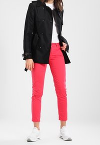 Černý trenčkot s dvouřadým zapínáním, růžové slim fit kalhoty a bílé tenisky. Trenčkot má knoflíky a kapsy.