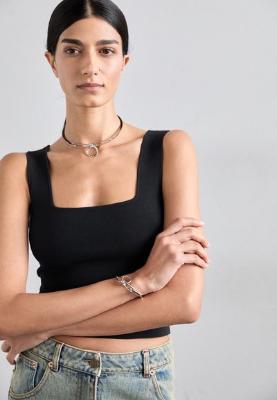 Black square-neck tank top made of textured fabric, paired with light blue high-waisted jeans. Silver choker necklace and bracelet.