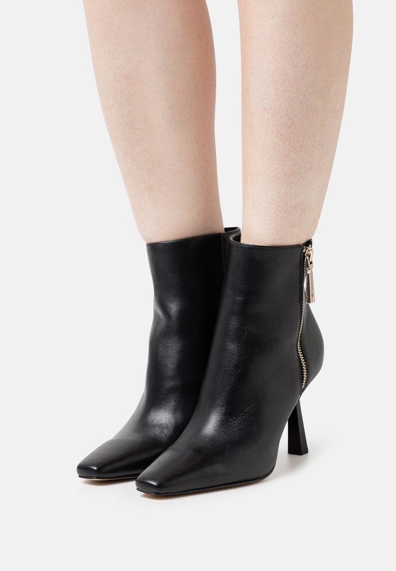 Botines de cuero negro con punteras puntiagudas, tacones delgados y cierre de cremallera con detalle metálico. Textura lisa.