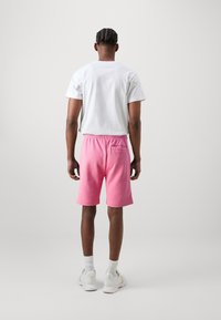 Biała koszula z krótkim rękawem w połączeniu z różowymi bawełnianymi szortami z elastycznym pasem i małą kieszonką z tyłu. Uzupełniona białymi trampkami.