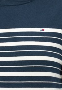Maglione blu navy con righe orizzontali bianche e un piccolo logo rettangolare in rosso, bianco e blu navy sul petto.