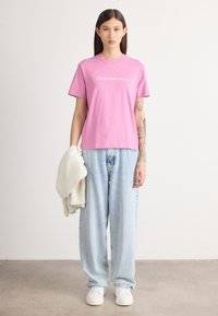 Rozā kokvilnas T-krekls ar īsām piedurknēm, ar baltu "Calvin Klein Jeans" logo. Apvienots ar gaiši ziliem platām kājām džinsiem un baltiem sporta apaviem.