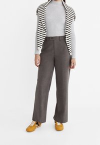 Szare spodnie o szerokich nogawkach wykonane z teksturowanej tkaniny, zestawione z prążkowanym szarym topem oraz czarno-biało paskowanym kardiganem zarzuconym na ramiona.