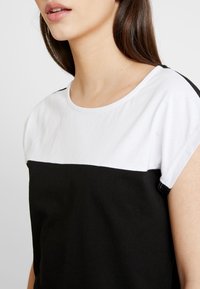 Czarny i biały krótki rękaw top z okrągłym dekoltem, z białą górną częścią i czarną dolną częścią. Miękka bawełniana tkanina.