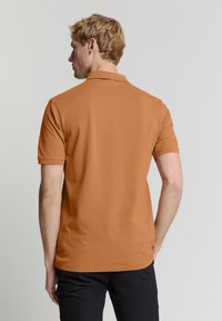 Bruine polo met korte mouwen, gemaakt van gladde katoenstof, met een klassieke kraag en een aansluitende silhouette aan de achterkant.