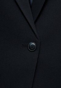 Musta bleiserikangas, jossa on sileä pinta, varustettuna kauluksella ja pyöreällä mustalla napilla edessä.