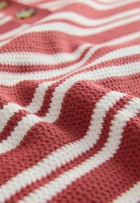 Gros plan sur un tissu texturé avec des rayures tricotées horizontales alternant rouge et blanc et trois boutons en bois sur un fond rouge.