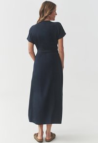 Abito maxi blu navy con maniche corte, texture morbida, vita aderente con cintura, e silhouette fluida, abbinato a mocassini marroni.