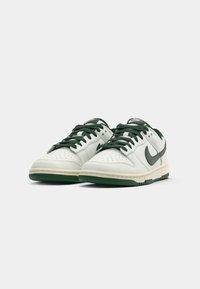 Pár bielych a tmavozelených nízkych tenisiek Nike s šnúrkami, perforovanou špičkou a gumovými podrážkami na jednoduchom pozadí.