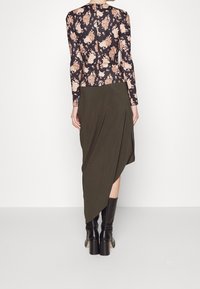 Top a maniche lunghe floreale in bianco e beige, abbinato a una gonna asimmetrica verde oliva scuro, indossato con stivali neri con tacco.