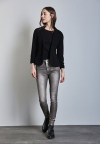 Svart blazer med uppvikta ärmar, kombinerad med en figurnära svart topp och metallic silverfärgade smala jeans. Svarta ankelskor fulländar outfiten.