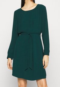 Zielona sukienka z długim rękawem, wykonana z miękkiego, lekkiego materiału. Posiada okrągły dekolt oraz materiałowy pasek, który podkreśla sylwetkę.