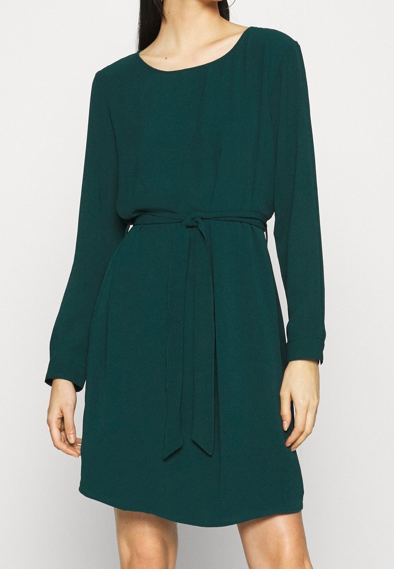 Zielona sukienka z długim rękawem, wykonana z miękkiego, lekkiego materiału. Posiada okrągły dekolt oraz materiałowy pasek, który podkreśla sylwetkę.