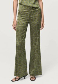 Pantalons évasés en tissu vert olive avec un motif g�éométrique en bleu foncé et blanc. Associés à des sandales noires à brides.