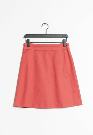 Korallinen vaaleanpunainen A-linjainen hame, jossa on hienovarainen tekstuuri, roikkuu mustassa klipsihangessa valkoista taustaa vasten.