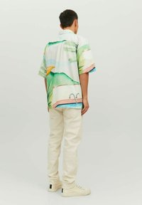Camicia a maniche corte con colletto, caratterizzata da un motivo paesaggistico astratto e colorato. Tessuto leggero e morbido. Abbinata a pantaloni color crema e sneakers.