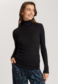 Schwarzes, geripptes Rollkragenoberteil mit langen Ärmeln, aus einem dehnbaren Stoff gefertigt. Kombiniert mit gemusterten, locker sitzenden Hosen in Blautönen.