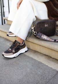 Hnědé a černé tenisky s meshovými a koženými akcenty, silnou bílou podrážkou a detailním kováním; hnědá crossbody taška s logem a vzorovaným popruhem.