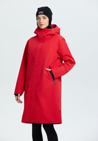 Lungo impermeabile rosso con colletto alto, tasche laterali e dettagli neri. Presenta un cappuccio con cordoncino e una silhouette dritta.