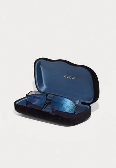 Prostokątne, niebieskawe okulary przeciwsłoneczne Gucci z wzorem GG na szkłach, w otwartym czarno-niebieskim aksamitym etui.