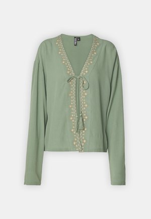 Grønn kortermet bluse i lett stoff, med V-hals, knyteinngang og broderte blomsterdetaljer langs fronten. Lange ermer.