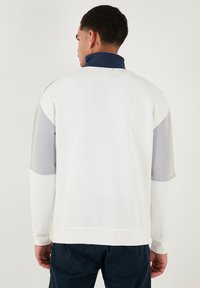 Valge fliisi sweatshirt hallide ja tumesiniste aktsentidega, kõrge krae, kerge kangas, ribidega varrukad ja lõdva lõikega.