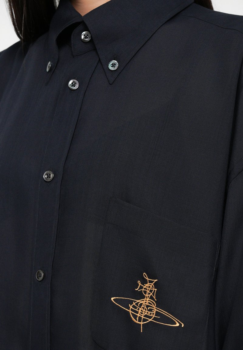 Marineblaues Hemd aus leichtem Stoff mit spitzem Kragen, ausgestattet mit einer Brusttasche, die mit goldener Stickerei eines geometrischen Designs verziert ist.