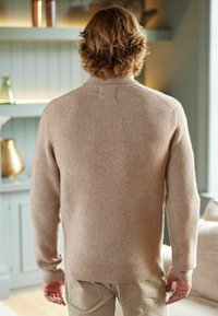 Suéter beige de punto acanalado con mangas largas y cuello alto simulado, con un ajuste relajado y una textura sutil. Vista trasera mostrada.