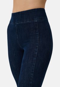 Leggings blu scuro con una cintura larga e elastica. Il tessuto presenta una superficie liscia con un leggero dettaglio simile al denim. Nessuna tasca visibile.