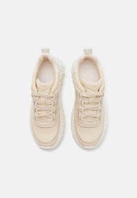 Beige joggesko med en glatt læroverdel, teksturert gummisåle og polstret pløse. Har snøring og en subtil logo på pløsen.