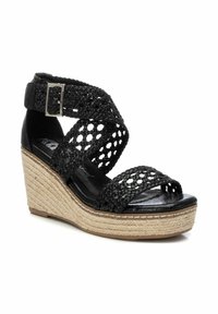 Sandalias de cuña negras con parte superior trenzada, punta abierta y correa en el tobillo. El talón envuelto en yute añade textura; planta de cuero suave para mayor comodidad.