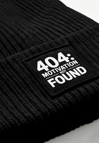 Black knitted beanie with a rectangular patch featuring white text that reads "404: MOTIVATION NOT FOUND." Text contrasts with the fabric texture.