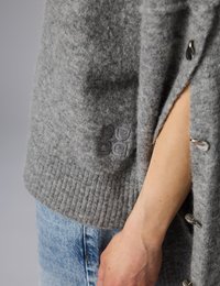 Gros plan sur le bras d'une personne portant un cardigan en laine grise avec des boutons à bascule en métal et un jean en denim bleu.