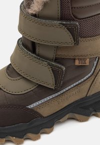 Brązowe i oliwkowe wodoodporne buty z dwoma paskami na rzep, teksturowanym materiałem wierzchnim i solidną gumową podeszwą. Zawierają etykietę marki "bisgaard."