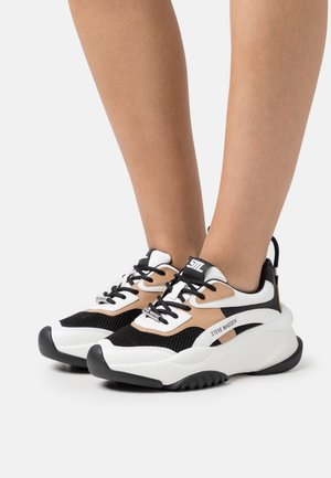 Baskets noires, blanches et fauves avec une tige en mesh, une semelle épaisse et un laçage. Marque notable sur le côté. Coupe régulière.