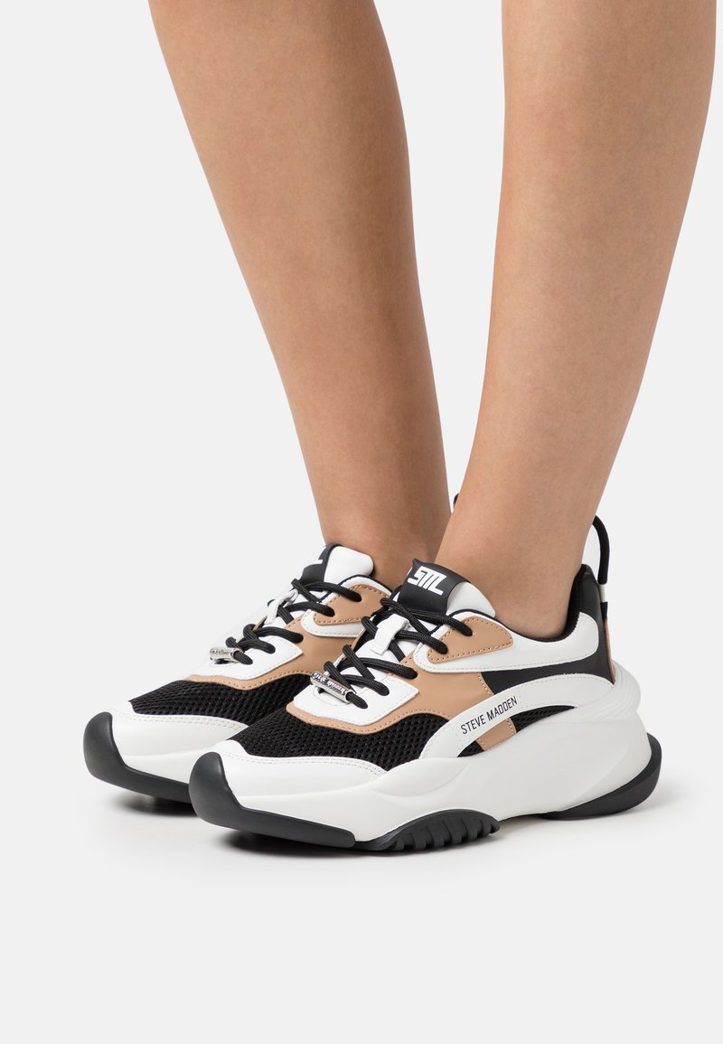 Baskets noires, blanches et fauves avec une tige en mesh, une semelle épaisse et un laçage. Marque notable sur le côté. Coupe régulière.