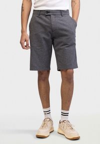 Grå houndstooth shorts med forlommer, bæltestropper og knaplukning. Stylet med hvide sokker og beige sneakers.