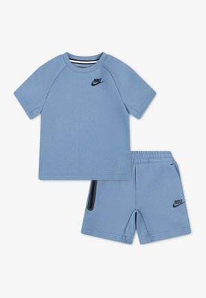 Svetlo modra otroška majica kratkih rokavov in kratke hlače z elastičnim pasom znamke Nike, z črnimi logotipi Swoosh in črnimi poudarki na žepu hlač.