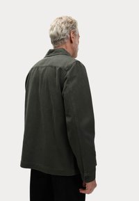 Dark green cotton jacket with a collar, buttoned cuffs, and a relaxed fit. Features a smooth texture and visible stitching details.