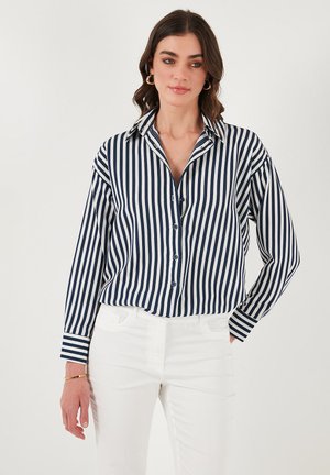 Navy and white striped long-sleeve button-up shirt with a collar, features a relaxed fit and cuffed sleeves. Paired with white pants.