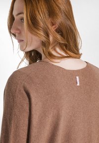 Brauner Strickpullover mit einer weichen Textur, ausgestattet mit einem runden Halsausschnitt und einem kleinen rosa Markenlabel auf der Rückseite.