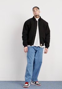 Black bomber jacket, white t-shirt, light blue baggy jeans, red and white sneakers with black accents. Simple design, casual fit.