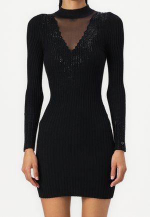 Czarna prążkowana mini sukienka dzianinowa z długimi rękawami, wysokim kołnierzem oraz przezroczystym panel V-kształtnym z siateczki z falowanym brzegiem na wysokości piersi.