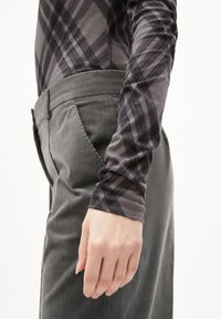 Grijs longsleeve shirt met zwart geruit patroon, gecombineerd met grijze corduroy broek met verticale ribbeling. Eenvoudige handbeweging zichtbaar.