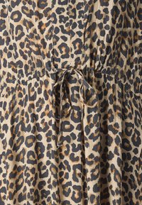 Šaty s leopardo vzorom v béžovej a čiernej farbe, s textúrovanou tkaninou, zhlukovaným pásom s viazaním a rôznymi vzormi leopardích škvŕn.
